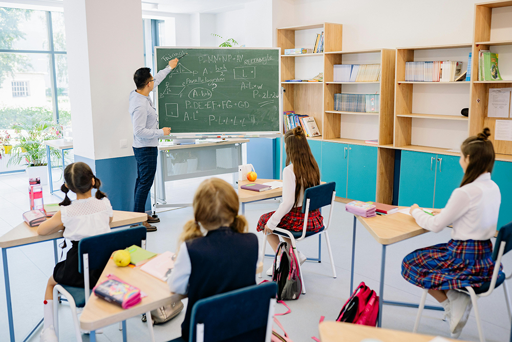 Students learning in a bright classroom with teacher writing on chalkboard