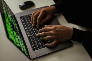 Hands typing code on a laptop for cyber security.