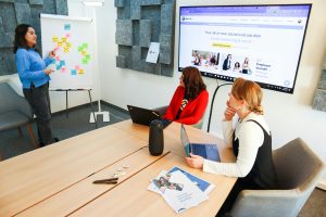 Team collaborating in a small meeting room with a screen and whiteboard.