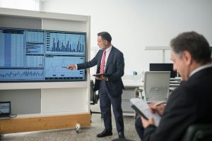Business presenter pointing to charts on a large display in a meeting room