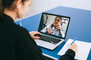 Person attending an online video meeting on a laptop while taking notes